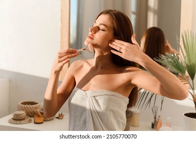 Portrait of a beautiful woman wrapped in a white towel to massage her face with a Y-shaped ball roller. Natural cosmetics concept, wrinkle smoothing