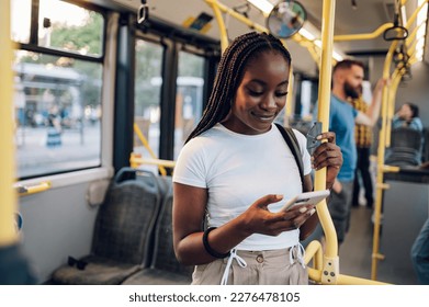 Portrait of a beautiful young African american woman using a smartphone while standing alone on a bus. Traveling to work and enjoying a bus ride. Black female using public transportation. Copy space.