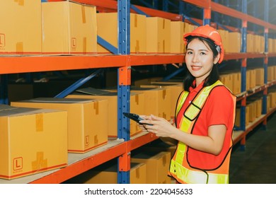 Portrait Beautiful Young Asian Female Worker Working The Night Shift Wearing A Helmet Works With Smiling Face, Use Tablet To Inspect The Boxes From The Warehouse Shelf To Verify They Are Correct.