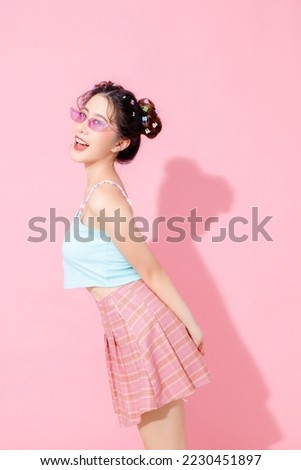 Portrait of beautiful young Asian happy woman in blue cute fashion dress wear sunglass smiling and posing on isolated pastel pink color background empty space.