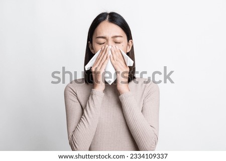 Portrait of beautiful young asian sick woman over isolated white background being wrapped in scarf sneezing, suffering from runny nose and high temperature. Cold and fever concept.