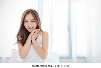 Portrait of beautiful young asian woman with attractive smile enjoy fresh bedding linen mattress in white bed room apartment. Teenage asia girl sleep resting, good night sleep facial skincare concept.