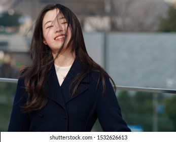 Portrait Of Beautiful Young Asian Woman With Black Long Hair, Smiling And Happy In Wind With Blur Background.