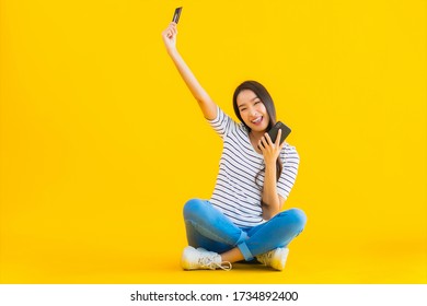 Portrait beautiful young asian woman smile happy use smart mobile phone on yellow isolated background - Shutterstock ID 1734892400