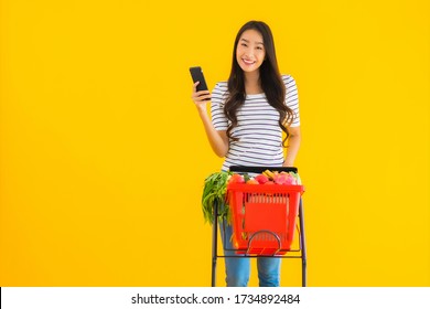 Portrait Beautiful Young Asian Woman Shopping Grocery From Supermarket And Cart With Smart Mobile Phone On Yellow Isolated Background