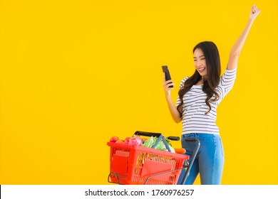 Portrait Beautiful Young Asian Woman Shopping Grocery From Supermarket And Cart With Smart Mobile Phone On Yellow Isolated Background