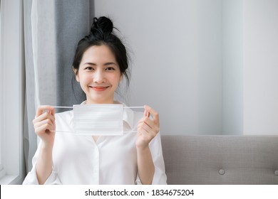 Portrait of beautiful young asian woman holding a medical mask stay alone at home for self quarantine. coronavirus outbreak situation concept. - Powered by Shutterstock