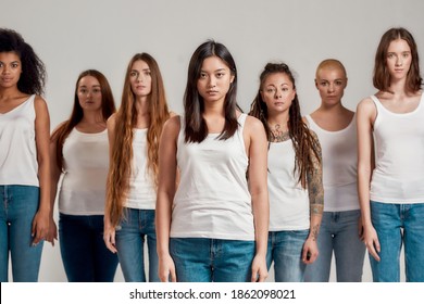 Portrait of beautiful young asian woman in white shirt looking at camera. Group of diverse women standing isolated over grey background. Diversity concept. Front view. Selective focus