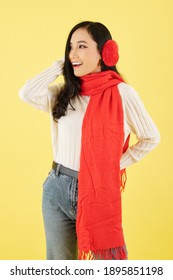 Portrait Of Beautiful Young Asian Woman In Red Ear Muffs And Scarf Standing Against Yellow Background