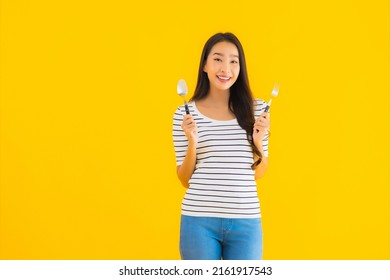 Portrait beautiful young asian woman show spoon and fork ready to eat on yellow isolated background
