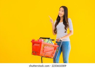 Portrait beautiful young asian woman shopping grocery from supermarket and cart on yellow isolated background - Shutterstock ID 2233610309