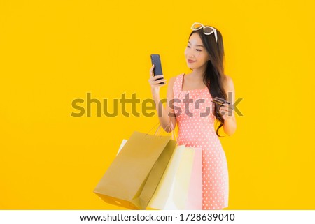Portrait beautiful young asian woman with colorful shopping bag with smart mobile phone and credit card on yellow isolated background