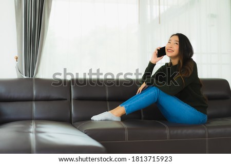 Portrait beautiful young asian woman use smart mobile phone or cellphone on sofa in living room interior