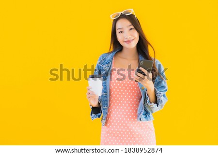 Portrait beautiful young asian woman with coffee cup and smart mobile phone on yellow isolated background