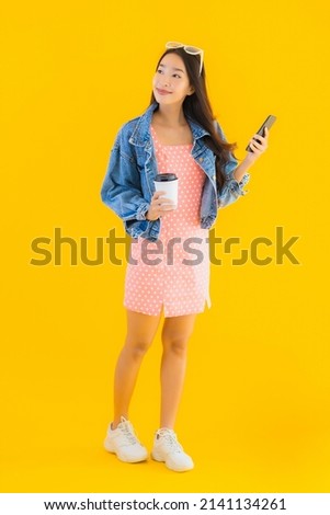 Portrait beautiful young asian woman with coffee cup and smart mobile phone on yellow isolated background