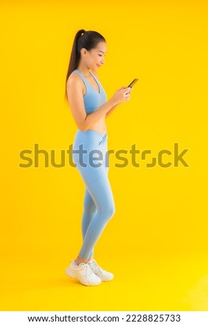 Portrait beautiful young asian woman wear sportwear with smart mobile phone on yellow isolated background