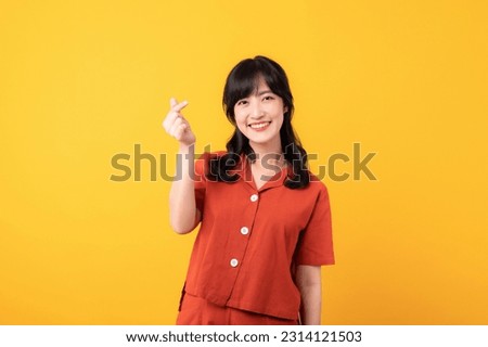 Portrait beautiful young asian woman happy smile dressed in orange clothes showing mini heart hand gesture isolated on yellow studio background.