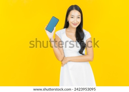 Portrait beautiful young asian woman smile with smart mobile phone on yellow color background