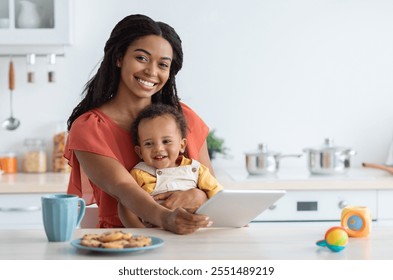 Portrait Of Beautiful Young Black Mom And Cute Infant Child Using Digital Tablet In Kitchen, Smiling African American Mother Holding Her Adorable Toddler Kid And Relaxing With Modern Gadget At Home - Powered by Shutterstock