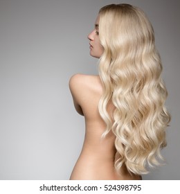 Portrait Of A Beautiful Young Blond Woman With Long Wavy Hair. Back View