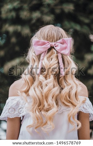 Portrait Of A Beautiful Young Blond Woman With Long Wavy Hair with pink bow. Back View. 
