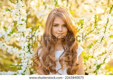 Portrait of beautiful young blonde curly girl with blue eyes posing on spring nature with white blooming trees.Sunny positive colorful photo with amazing teenage model. Light in hair.  
