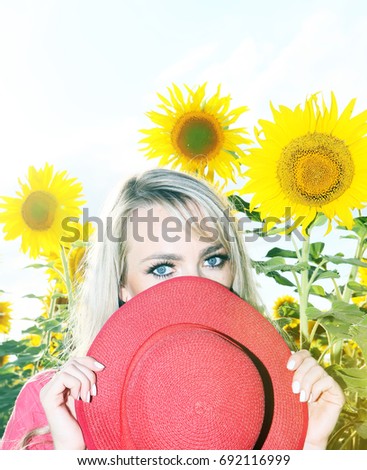 Portrait of Beautiful young blonde with the yellow of sunflowers, holding a pink summer hat