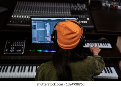 Portrait of beautiful young brunette, female artist playing keyboard synthesizer, sitting in recording studio - Powered by Shutterstock