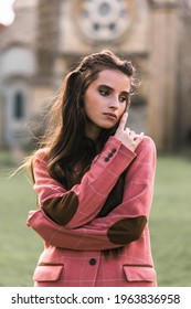 Portrait Of A Beautiful Young Brunette Girl, Model, In A Classic Checkered Pink Jacket With Elbow Patches. Thoughtful Look. Background Architecture.