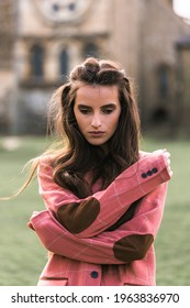 Portrait Of A Beautiful Young Brunette Girl, Model, In A Classic Checkered Pink Jacket With Elbow Patches. Thoughtful Look. Looking Down. Background Architecture.