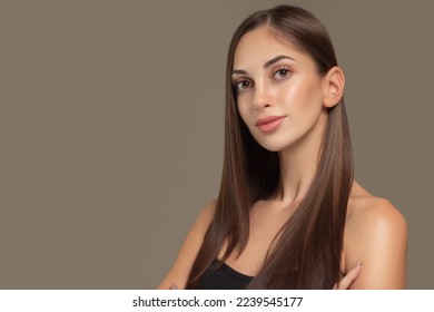 Portrait of a beautiful young brunette woman with long straight hair. On a gray background