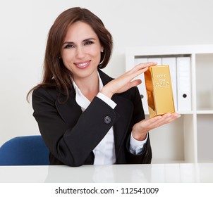Portrait of a beautiful young businesswoman holding gold bar at office desk - Shutterstock ID 112541009