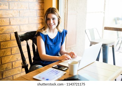 Portrait Of Beautiful Young Businesswoman Working On Laptop Computer At Restaurant And Making Eye Contact
