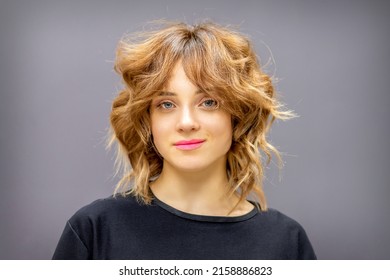 Portrait of a beautiful young caucasian red-haired woman with short wavy hairstyle smiling and looking at camera on dark gray background with copy space