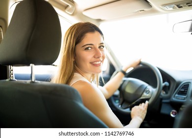 Portrait of beautiful young caucasian woman sitting in the driving seat of the car and looking back at the camera with a smile on her face - Shutterstock ID 1142769746