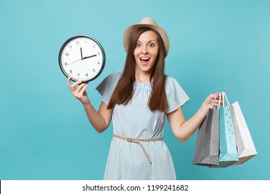 Portrait beautiful young caucasian woman in summer dress, straw hat holding packages bags with purchases after shopping, round clock isolated on blue pastel background. Copy space for advertisement