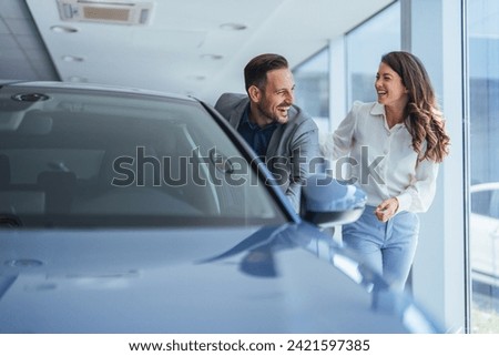 Portrait of a beautiful young couple choosing a new car at a car dealership. Buying a long-awaited car. Couple buying the automobile. Pair in a car salon. Husband with vife choose the automobile