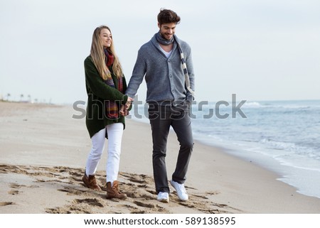 Portrait of beautiful young couple in love walking in a cold winter on the beach.