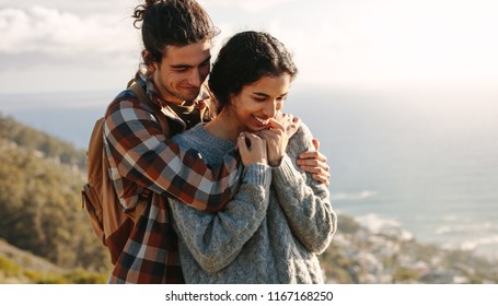 Portrait Of Beautiful Young Couple On A Vacation. Man Hugging His Girlfriend From Behind, Both Standing On A Cliff.