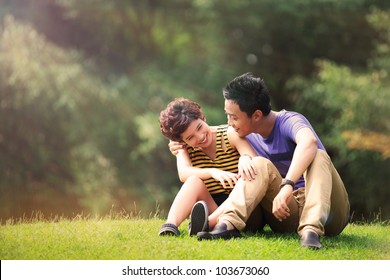 Portrait of beautiful young couple sitting on ground in park relaxing