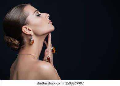 A portrait of a beautiful young dark-haired woman posing in the studio over the black background. Beauty, cosmetics, skincare, jewelry.