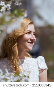 Portrait Of A Beautiful Young European Girl With Golden Loose Curls In A White Lace Dress Looks Away Smiling