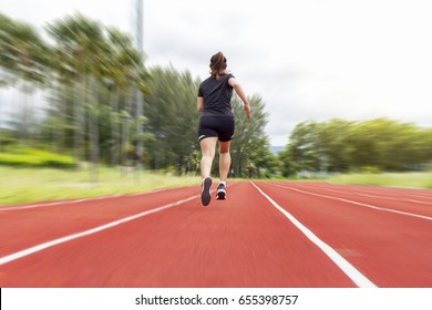 Portrait Of Beautiful Young Female Athlete Running On Running Track (back View) On Blur Background