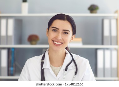 Portrait Of Beautiful Young Female Doctor Looking At Camera In Medical Office, Having Online Consultation With Patient