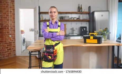 Portrait Of Beautiful Young Female Handyman In Overall And Tool Belt Standing In Home Kitchen And Smiling At Camera. Repairman Service And Female Hard Work Concept