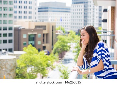 A Portrait Of A Beautiful Young Female Relaxing On A Balcony On A Sunny Summer Day, In Her New Apartment, Background Of A City Scenery And Green Trees. Urban Lifestyle. 