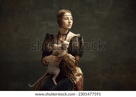 Portrait of beautiful young girl in elegant clothing over dark vintage background posing with sphynx cat. Lady with ermine remake. Concept of history, renaissance art remake, comparison of eras