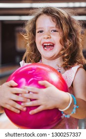 Portrait of a beautiful young girl with freckles smiling and holding a pink bowling ball. Father and daughter spending time together.