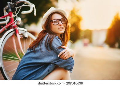 portrait of a beautiful young girl in a hat with a bicycle on city background in the sunlight outdoor