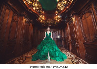 Portrait of a beautiful young girl in a Haute couture green dress standing in a luxurious wooden and bronze interior.
